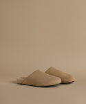 A pair of beige slip-on mule clog with a soft fuzzy lining, photographed on a clean, solid beige background.