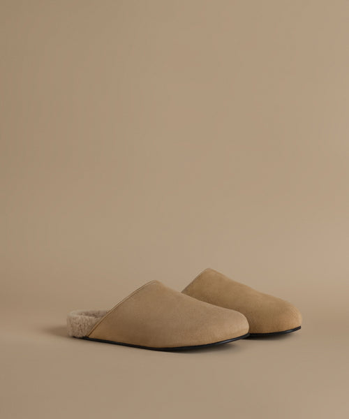 A pair of beige slip-on mule clog with a soft fuzzy lining, photographed on a clean, solid beige background.