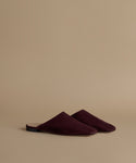 A pair of deep burgundy suede mule slippers on a solid beige background.