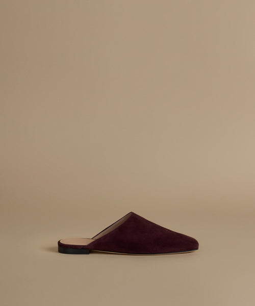 A single deep burgundy suede mule slipper shown in profile against a solid beige background.
