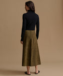 A woman shown from the back wearing a black long-sleeve turtleneck sweater and an olive green midi skirt, standing against a solid beige studio background.
