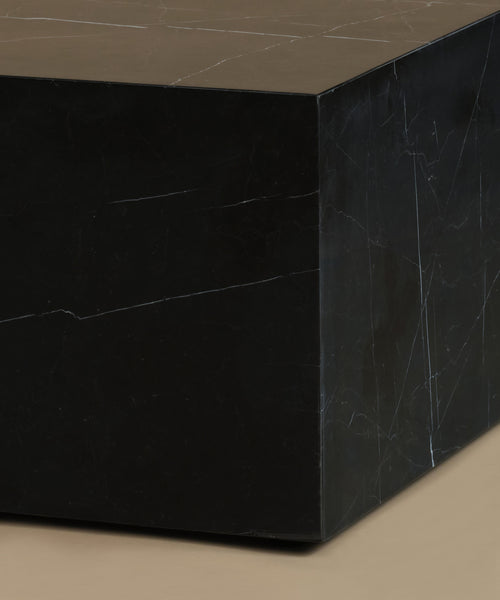 A close up of a rectangular black marble coffee table with white veining, set against a solid warm beige background.