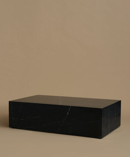 A rectangular black marble coffee table with white veining, set against a solid warm beige background.
