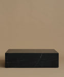 A rectangular black marble coffee table with white veining, set against a solid warm beige background.