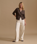Model wearing a brown cardigan with cream color jeans against a beige studio background.