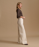 Model wearing a brown cardigan with cream color jeans against a beige studio background.