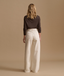 Model wearing a brown cardigan with cream color jeans against a beige studio background.