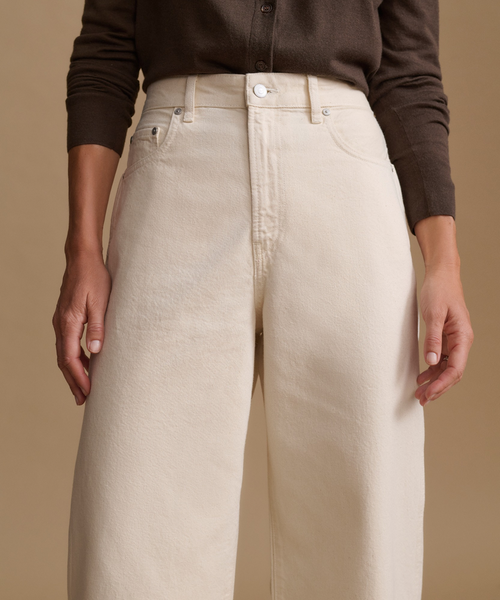 Model wearing a brown cardigan with cream color jeans against a beige studio background.