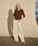 Model wearing a brown long-sleeve t-shirt with cream color jeans at the beach.