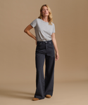 A woman modeling a pair of dark charcoal wide-leg jeans with a light gray t-shirt, standing against a solid beige studio background.