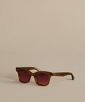 A pair of Thompson Sunglasses with brown, square frames and dark tinted lenses rests on a beige surface with a matching background, combining style and UV protection.