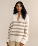 A woman with long dark hair wears the Cashmere Phoebe Polo, an ivory striped, soft jersey-knit cashmere sweater with a collar, paired with beige pants, standing against a plain light background.