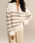 A person models the Cashmere Phoebe Polo—an ivory striped collared sweater—paired with beige pants, standing with one hand on their hip against a neutral backdrop.