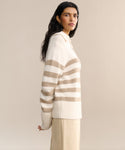 A woman with long dark hair wears the Cashmere Phoebe Polo in ivory stripes and a light beige skirt, standing against a plain beige background while looking toward the camera.