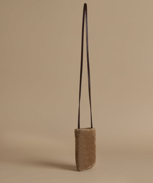 A small shoulder bag with a textured taupe-brown body and a dark brown leather strap, standing upright against a solid beige background.