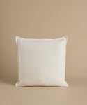 A white square pillow against a beige background.