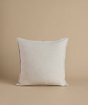 A cream square pillow against a beige background.