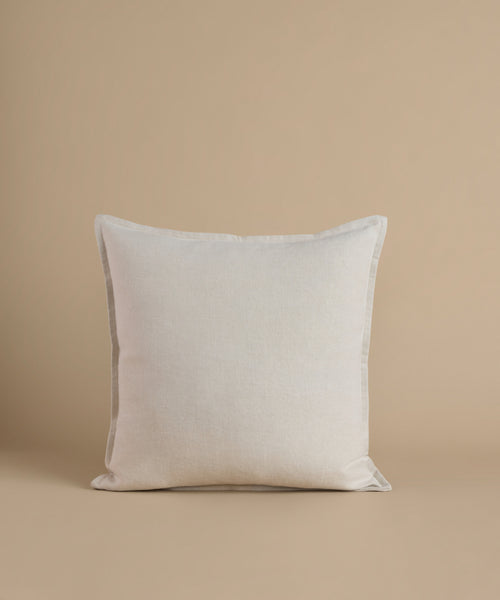A cream square pillow against a beige background.