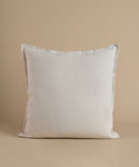 A cream square pillow against a beige background.