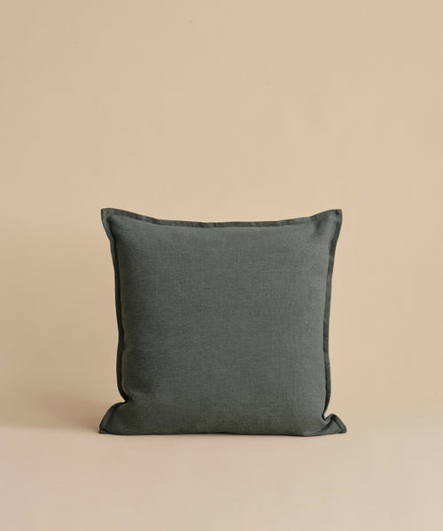 A dark gray Adler Pillow is centered against a beige background, showcasing its smooth Belgian linen cover. The luxury pillow appears plump and soft, highlighting its simple yet elegant design.