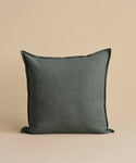 The Adler Pillow, featuring a square shape and soft Belgian linen texture in dark gray, is displayed upright against a plain beige background.