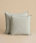 Two Adler Pillows in light gray linen blend rest against a beige background, with one slightly overlapping the other, capturing timeless Belgian-inspired style.