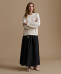 Woman wearing a cream cable knit sweater and black skirt on a beige background