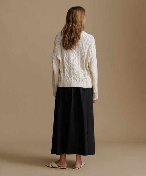 Woman wearing a white cable knit sweater and black skirt on a beige background