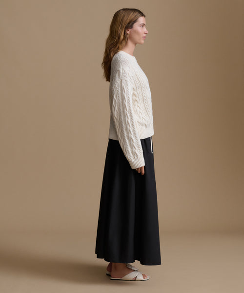 Woman wearing a white cable knit sweater and black skirt on a beige background
