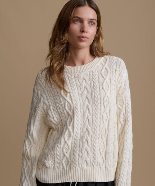 Woman wearing a cream cable knit sweater against a beige background