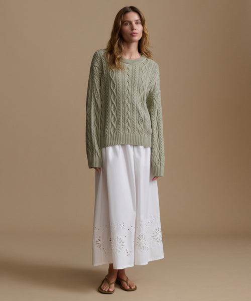 Woman wearing a green cable knit sweater and a white skirt on a beige background