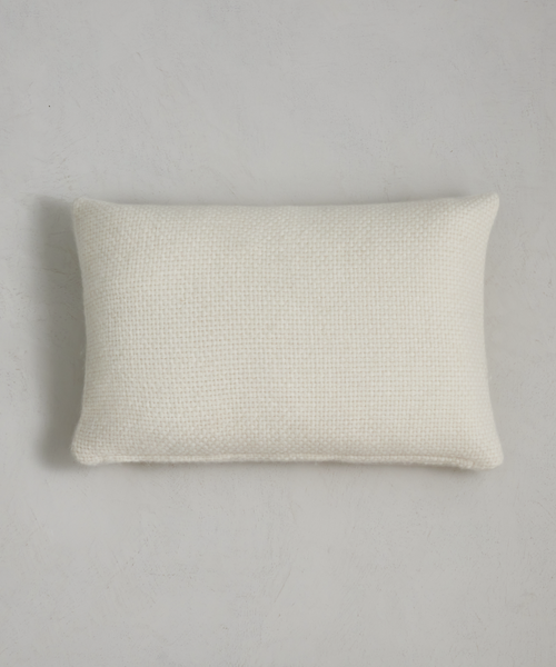 The Alpaca Basketweave Lumbar Pillow, rectangular and white with a soft woven texture, rests on a light gray surface, casting a slight shadow to the left.