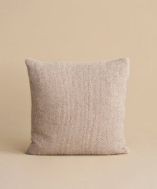 The Alpaca Basketweave Pillow, featuring a textured woven design and handmade in Peru, stands upright against a plain, neutral beige background.