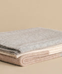 The Alpaca Colorblock Throw, handmade in Peru from soft wool in light grey, cream, and beige, is neatly folded and displayed on a beige surface against a neutral background.