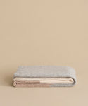 A neatly folded Alpaca Colorblock Throw in soft grey and beige rests on a neutral surface and matching background, highlighting the luxury of this handmade Peruvian piece.