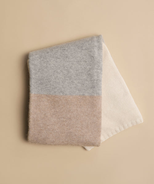The Alpaca Colorblock Throw, handmade in Peru, features soft woolen texture and three color blocks—light gray, light brown, and cream—beautifully displayed on a beige background for a luxurious look.