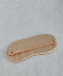 The Alpaca Eye Mask, made of beige silk with an elastic strap, rests on a light gray, textured alpaca wool surface.