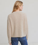 A woman with long blonde hair, seen from behind, wears the Hayes Crewneck Cardigan—a luxe fuzzy beige knit—paired with blue jeans against a plain light background.
