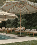 Black and white striped beach umbrella with chairs at a pool