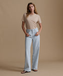 Woman wearing a beige t-shirt and light blue jeans against a brown background