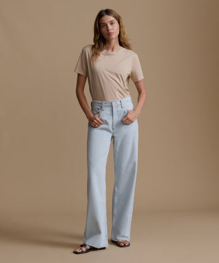 Woman wearing a beige t-shirt and light blue jeans against a brown background