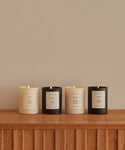 Four hand-poured candles, including the Aspen Glass Candle, are arranged on wood. Each comes in black or white jars with minimalist labels and is crafted from a natural wax blend in Los Angeles.