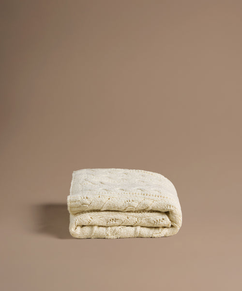 Folded beige cable knit blanket on a brown background