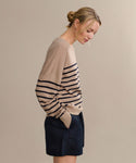 A woman with blonde hair in a low bun wears the Avery Crewneck striped sweater and dark shorts, standing in profile against a neutral background, hands in her pockets, for an effortless coastal look.