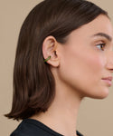 A woman with straight brown hair wears a small, green Bagel Ear Cuff on the outer edge of her left ear as she faces right against a beige background.