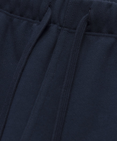Close-up of the Bay Sweatpant, featuring a navy blue brushed fleece fabric. The image highlights the waistband, drawstrings, visible stitching details, and the textured feel of these athletic sweats.
