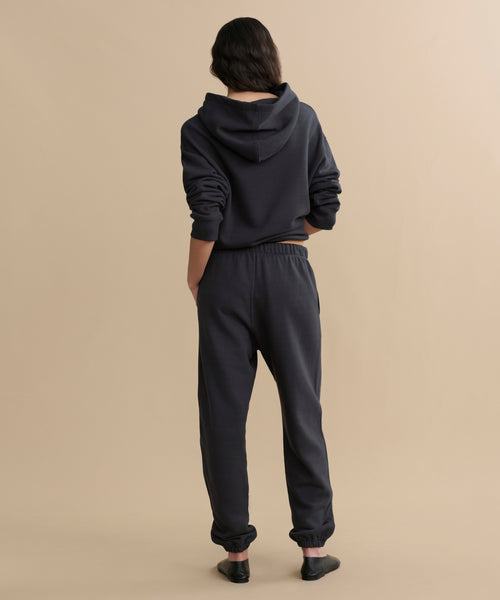 A person faces away from the camera in a dark hoodie and Bay Sweatpant athletic sweats against a plain beige background.