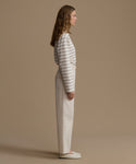 Woman wearing a striped shirt and white pants against a beige background