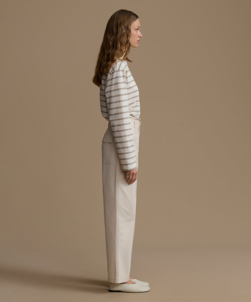 Woman wearing a striped shirt and white pants against a beige background