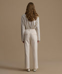 Person wearing a striped shirt and beige pants against a beige background